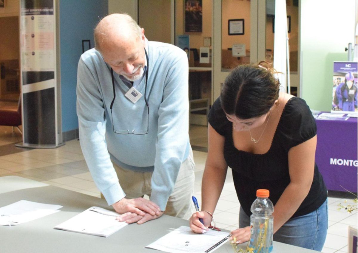 Rich Scheer, a League of Women Voters volunteer, assists Adriana Garcia, a nursing student, with her voter registration form.