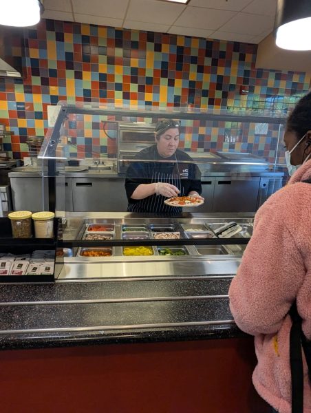 Chef Carmen Hernandez works behind the pizza station and prepares a layered pizza with a variety of toppings for a student’s carryout order in the Montgomery College kitchen on April 28.